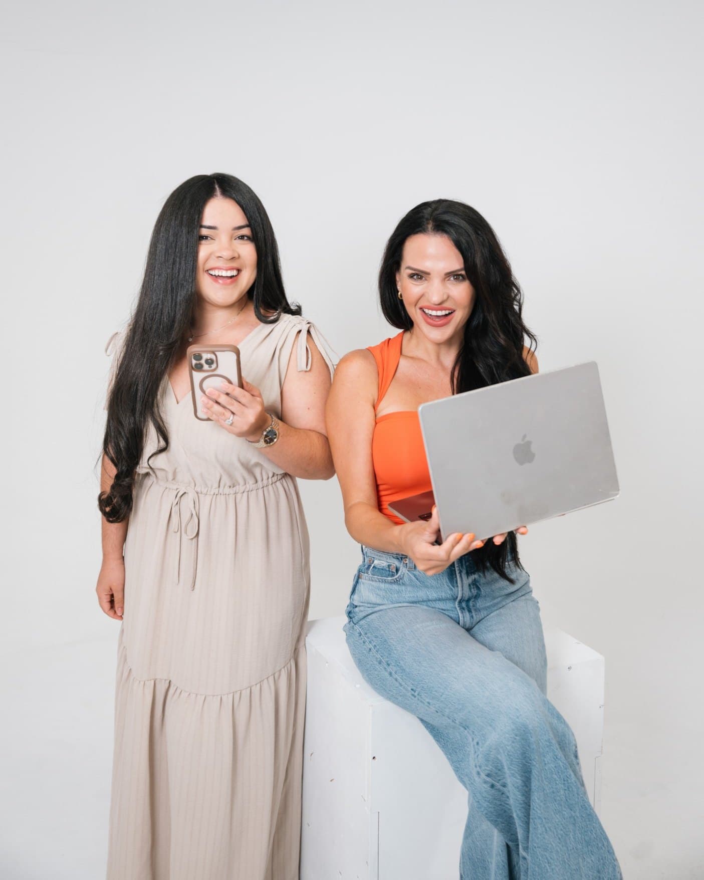 Luana and Nelly smiling in the studio, one holding a phone and the other a laptop